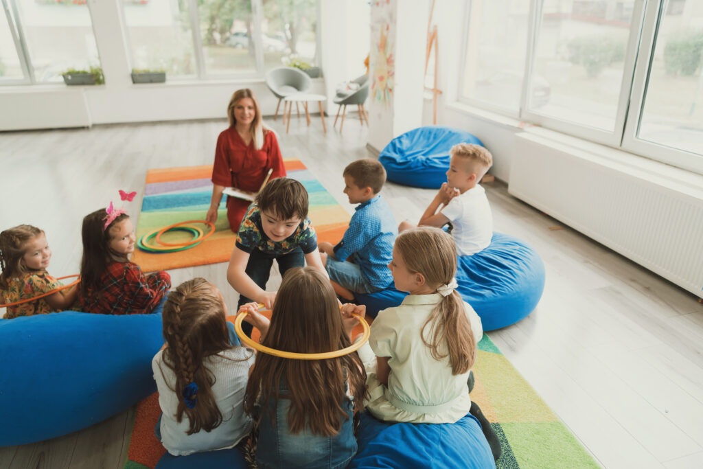 A happy female teacher sitting and playing hand games with a group of little schoolchildren