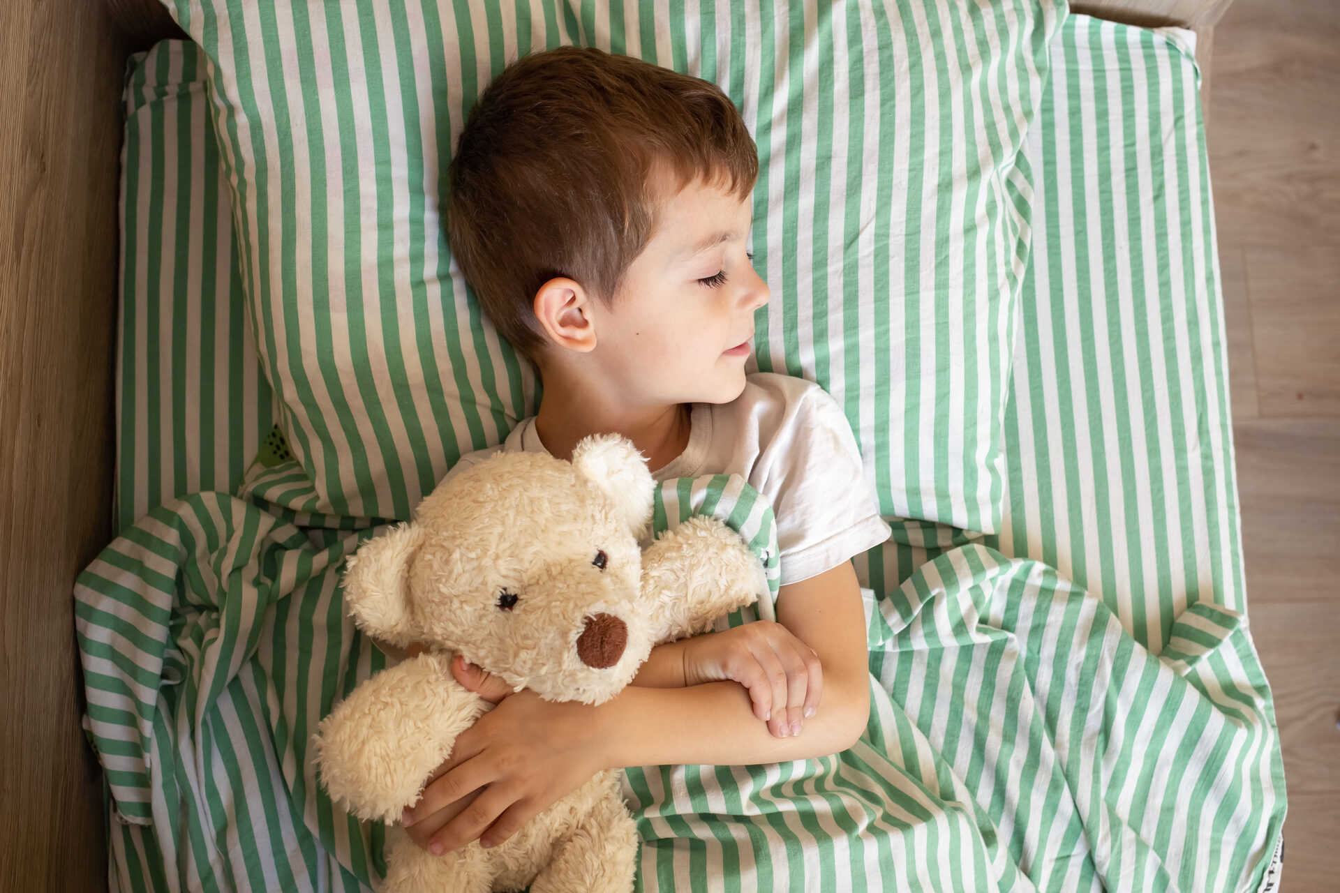 adorable boy sleeping in bed with bear toy.