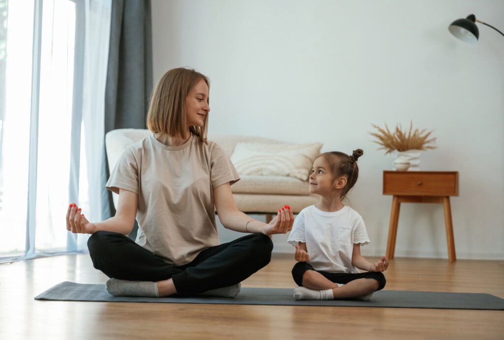 Young woman with little girl are doing yoga at home.