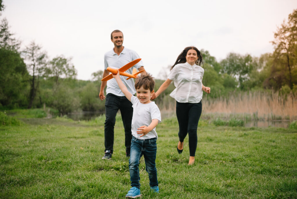 Father, mother and son playing with toy airplane in the park. friendly family. People having fun outdoors. Picture made on the background of the park and blue sky. concept of a happy family.