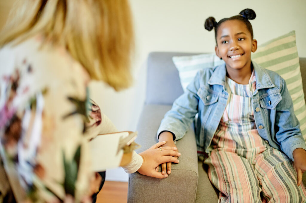 Child psychologist, holding hands and smile with girl for support, care or happiness for progress together. Happy female kid, childhood psychology and consultation for mental health for anxiety help.