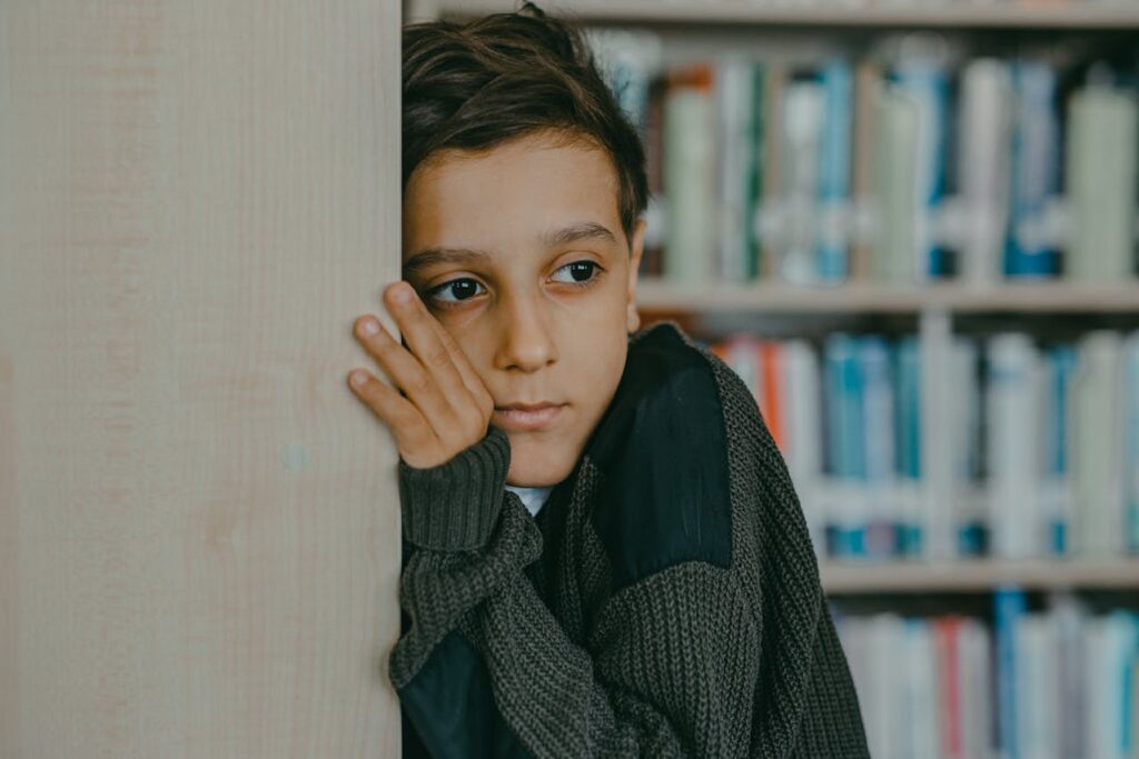 A contemplative child leans against a wall in a library, deep in thought.