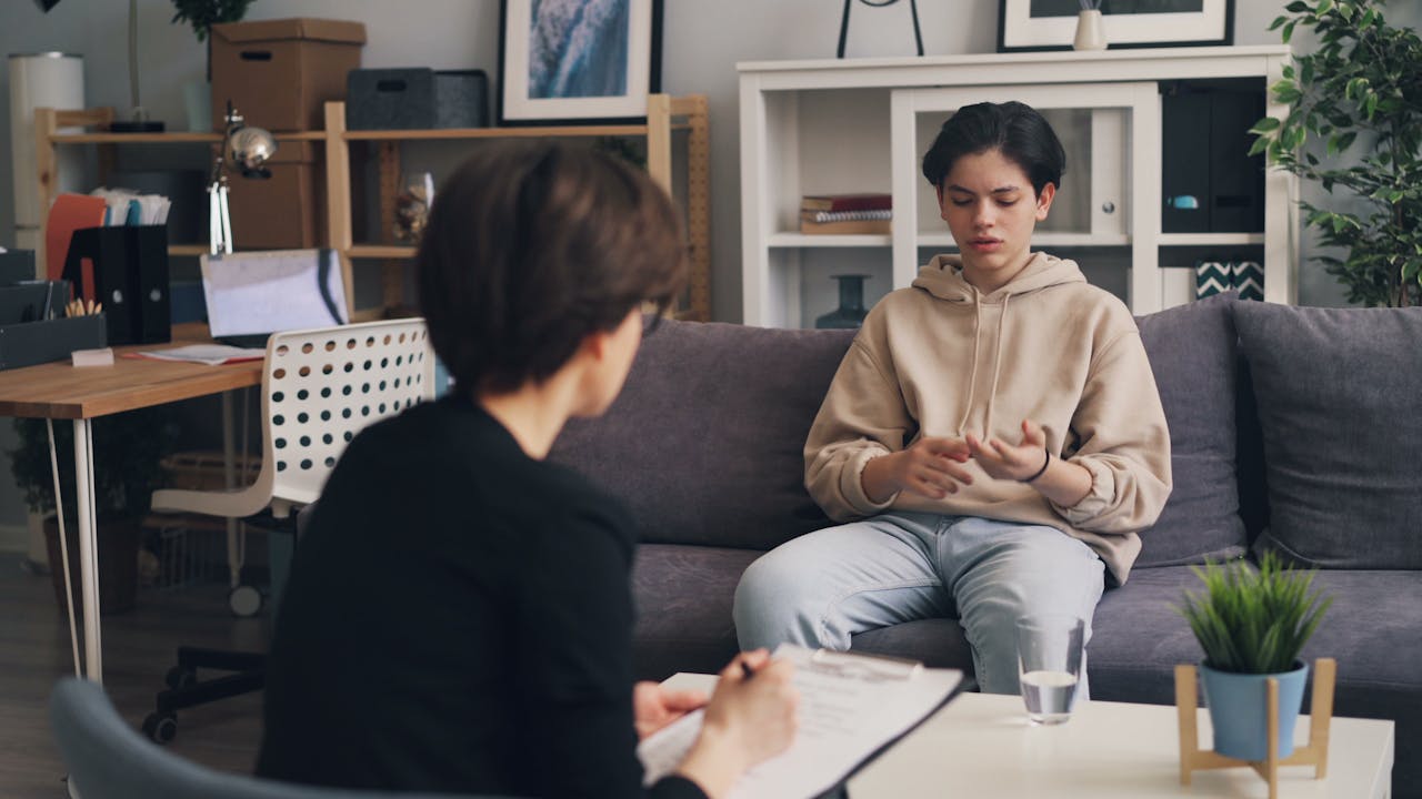 A teenager engages in a therapy session with a professional counselor in a modern office setting.